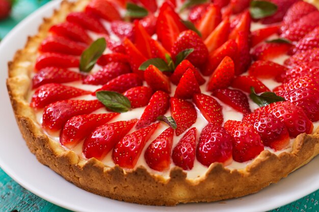 Tart with strawberries and whipped cream decorated with mint leaves.