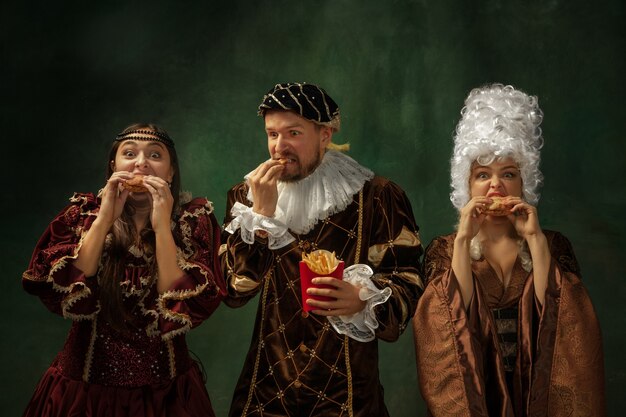 Taste of future. Portrait of medieval young people in vintage clothing on dark background. Models as a duke and duchess, princess, royal persons. Concept of comparison of eras, modern, fashion.