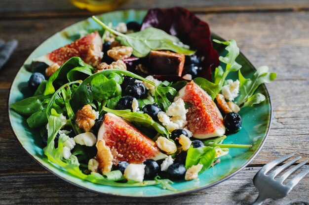 Tasty appetizing autumn salad with figs blueberries cheese nuts and arugula served on plate on dark background.