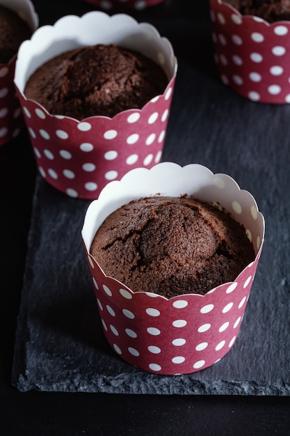 Free photo tasty appetizing chocolate muffins in cups on dark background.