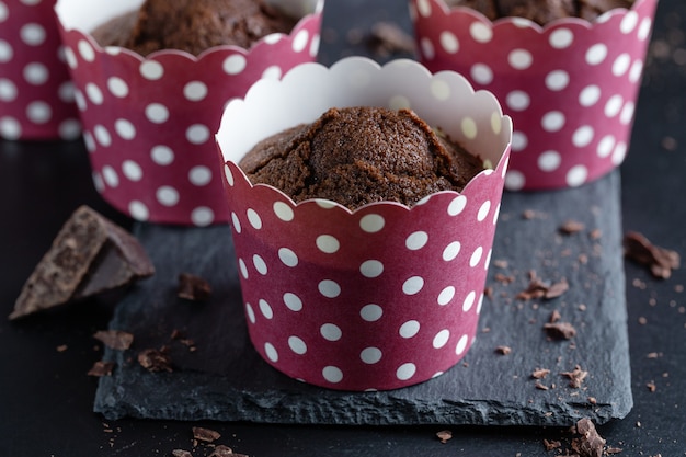Muffin al cioccolato appetitosi gustosi in tazze su sfondo scuro.