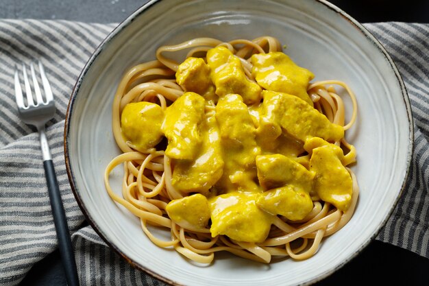 Tasty appetizing noodles spaghetti udon with chicken chunks in curry sauce served on plate. Closeup.