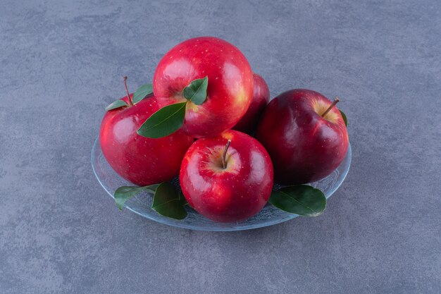 Вкусные яблоки на стеклянной тарелке на темной поверхности