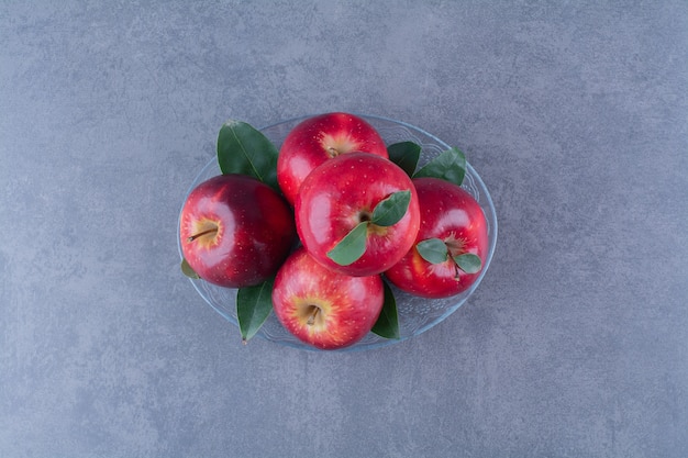 Вкусные яблоки на стеклянной тарелке на мраморном столе.
