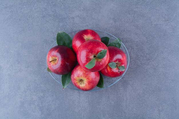 Вкусные яблоки на стеклянной тарелке на мраморном столе.
