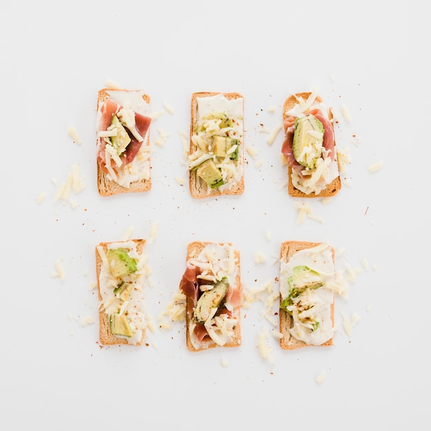Tasty arranged toasts with cheese; avocado and bacon on white background