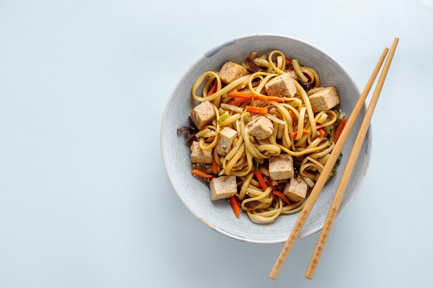 Tasty asian noodles with cheese tofu and vegetables on plates. Horizontal.