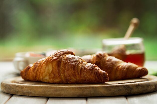 Tasty beautiful croissants on wooden board. Traditional continental breakfast. Granola with fruits and honey on background.
