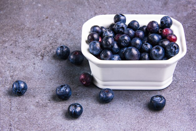 Tasty blueberries in a white square bowl on violet plaster background, side view.