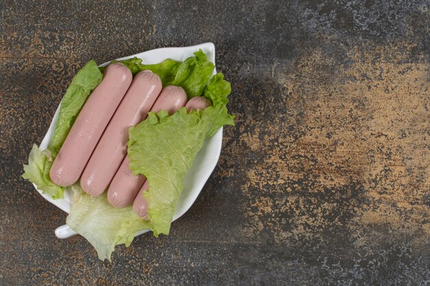 Tasty boiled sausages and lettuce on leaf shaped plate.