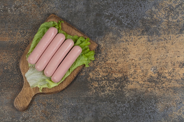 Foto gratuita gustose salsicce bollite e lattuga su tavola di legno.