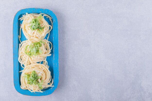 Вкусные вареные спагетти с зеленью на синей тарелке.
