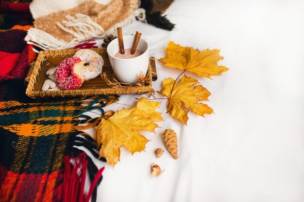 tasty breakfast in bed on wooden tray with cup of cacao, cinnamon, cookies and glazed donuts.