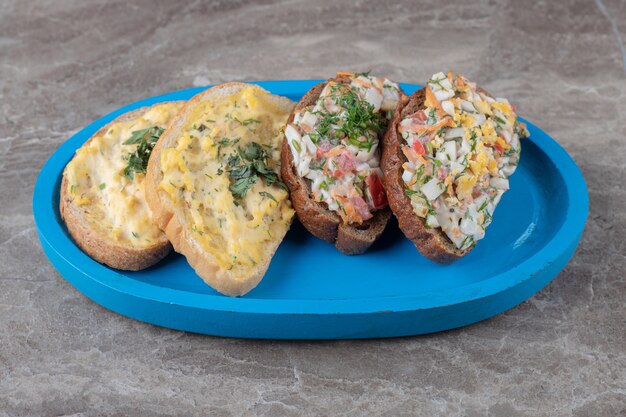 Tasty bruschettas with eggs and vegetables on blue plate.