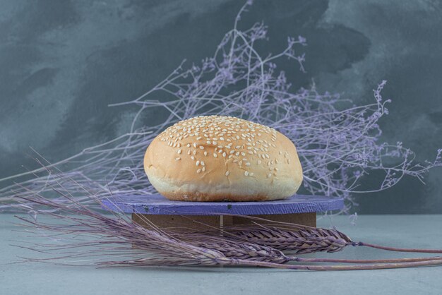 Tasty burger bun with sesame seeds on wooden board