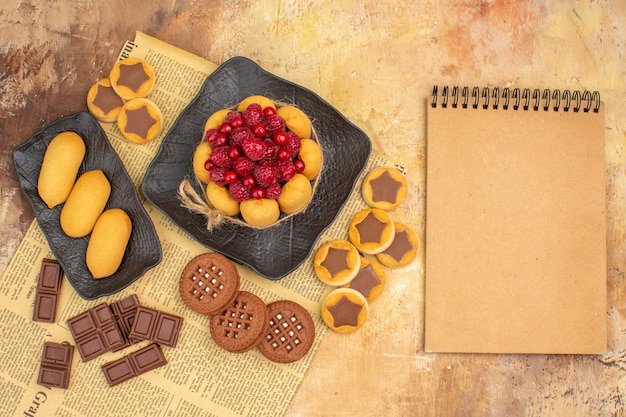 Вкусный торт с различным печеньем на коричневой тарелке и блокнот на столе смешанных цветов
