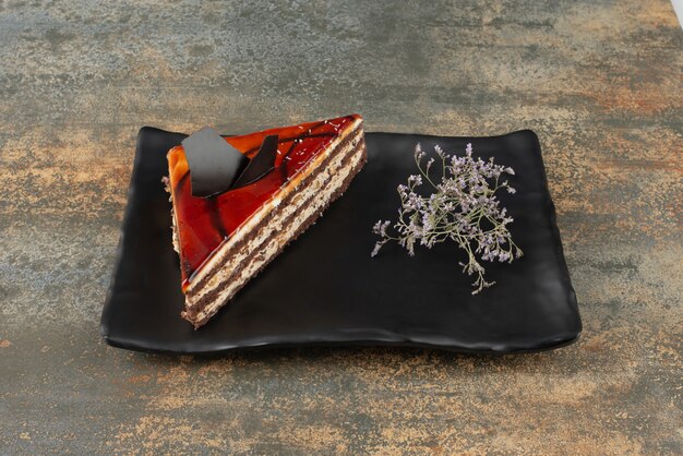 Tasty cake on plate with flower on marble surface.