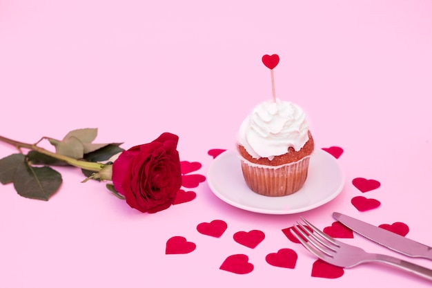 Tasty cake with whip between decorative hearts near flower