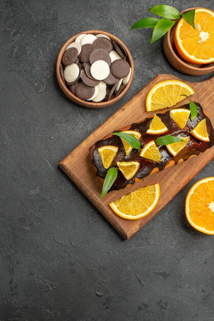 Tasty cakes cut oranges with biscuits on cutting board on dark table