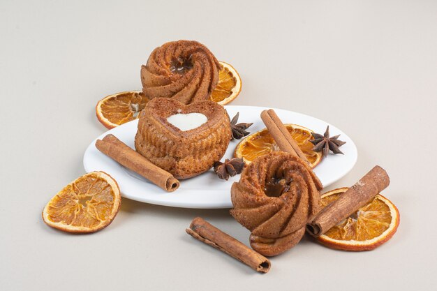 Tasty cakes with orange slices, cloves and cinnamon on white plate