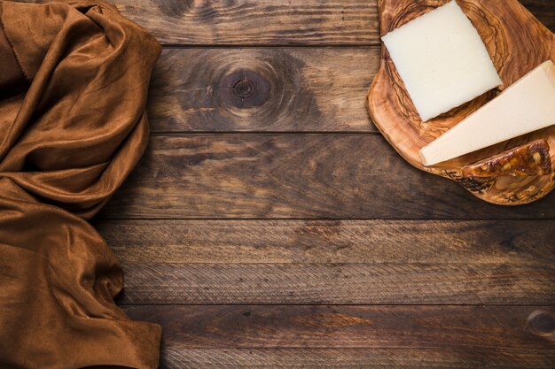 Tasty cheese on wooden cheese board with brown silk fabric over old wooden surface