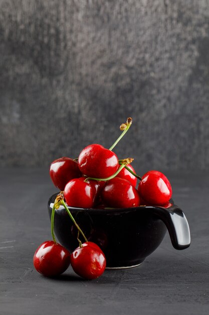 Tasty cherries in a black scoop on grungy and grey table, side view.