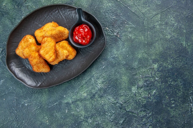 Tasty chicken nuggets and ketchup in black plates on the right side on dark surface