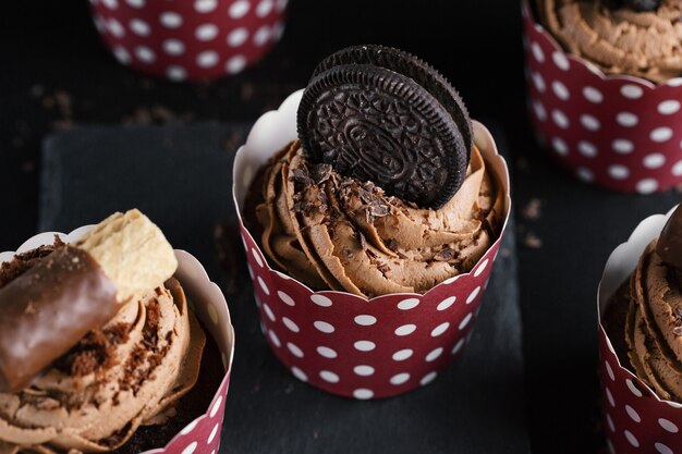 暗い背景のカップで飾られたバタークリームとおいしいチョコレートマフィンカップケーキ。閉じる