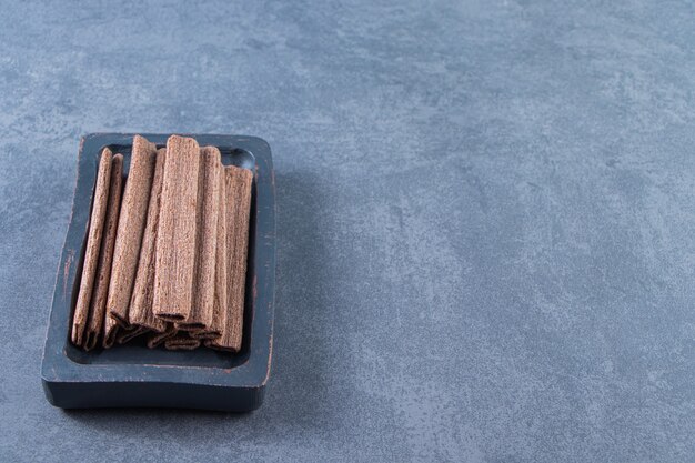 Tasty chocolate wafer roll in a wooden plate , on the marble background.