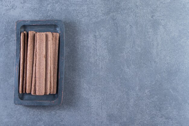 Вкусный шоколадный вафельный рулет в деревянной тарелке на мраморном фоне.