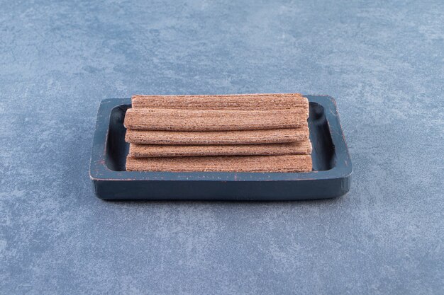 Tasty chocolate wafer roll in a wooden plate on the marble surface