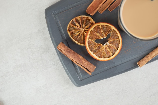 Free photo tasty coffee, cinnamon sticks and orange slices on dark plate.