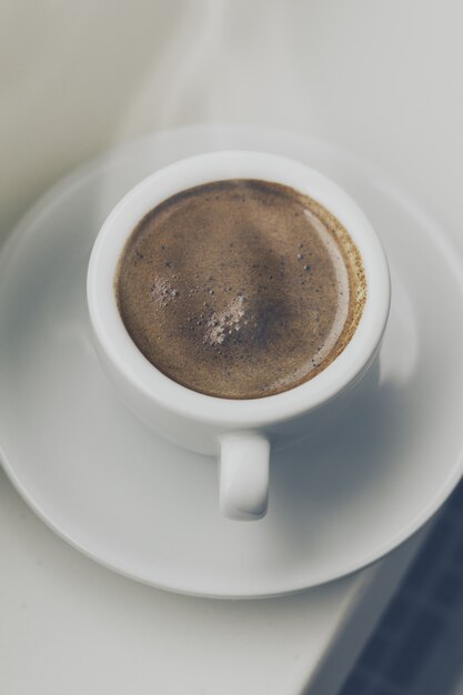 窓のそばの小さなカップに入ったおいしいコーヒーエスプレッソ。ホームコンセプト。上面図。トーニング