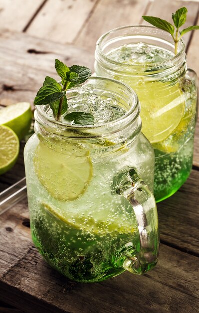 Tasty cold fresh drink lemonade with lemon, mint, ice and lime in glass on wooden table. Closeup.