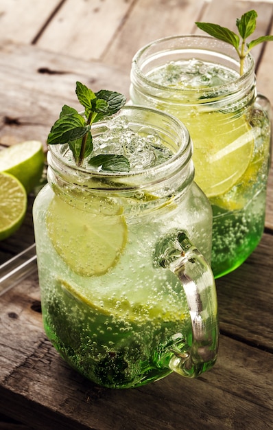 Tasty cold fresh drink lemonade with lemon, mint, ice and lime in glass on wooden table. Closeup.