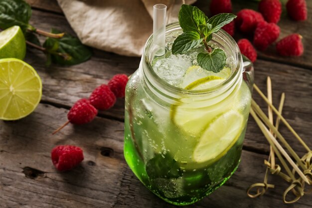 Tasty cold fresh drink lemonade with lemon, mint, raspberry, ice and lime in glass on wooden table. Closeup.