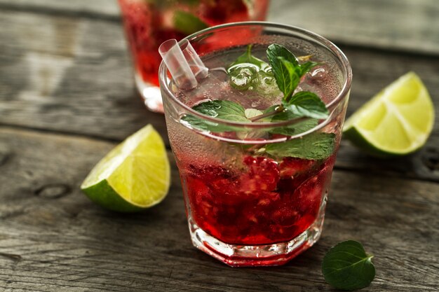 Tasty cold fresh drink lemonade with raspberry, mint, ice and lime in glass on wooden background. Closeup.