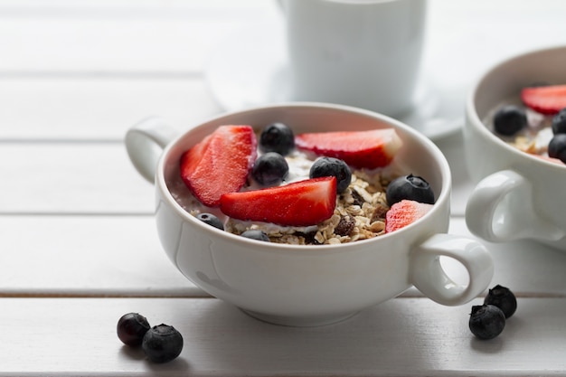 Colazione colorata gustosa con farina d'avena, yogurt, fragola, mirtillo, miele e latte su sfondo bianco di legno con lo spazio di copia. avvicinamento.