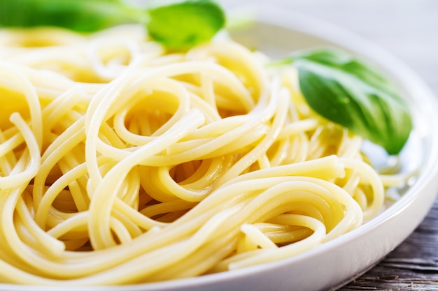 Tasty cooked colorful spaghetti pasta with fresh basil on plate on wooden background, closeup.