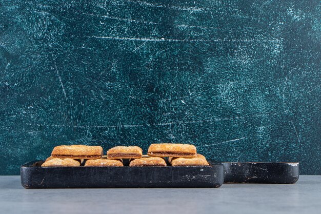 Tasty cracker biscuits filled with chocolate on black cutting board.