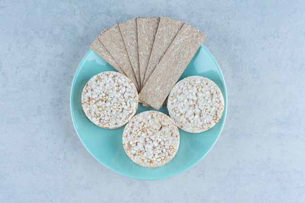 Вкусный крекер и воздушные рисовые лепешки в тарелке на мраморе.