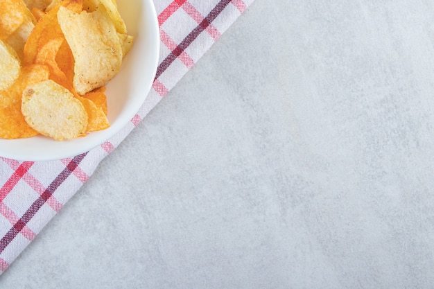 Tasty crispy chips placed in white bowl with tablecloth.