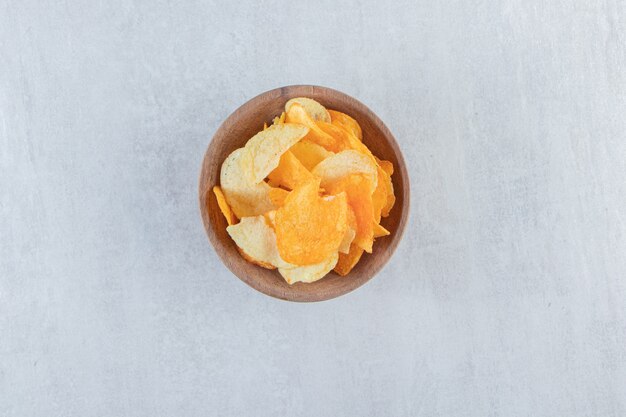 Tasty crispy chips placed in wooden bowl on stone.