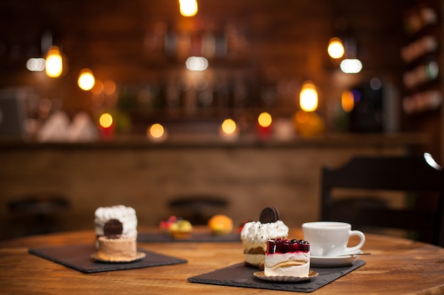 Tasty cup of coffee new delicious mini cakes with different shapes over a wooden table in a coffee shop