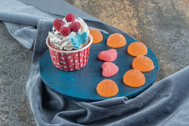 Tasty cupcake decorated with cream and candies on blue board