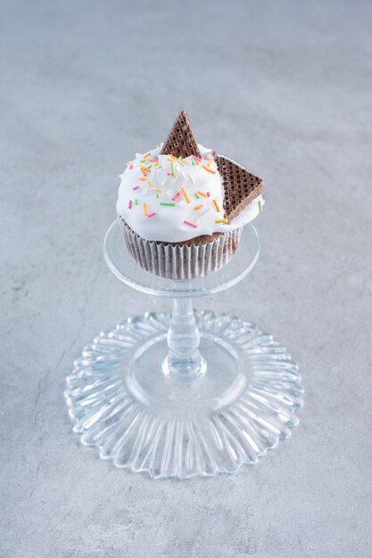 Free photo tasty cupcake decorated with cream and sprinkles on glass plate.