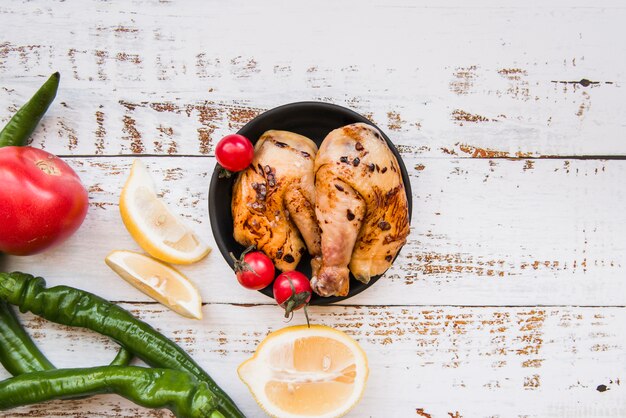 Tasty delicious roasted chicken in bowl with lemon; tomato; green chilies on wooden desk