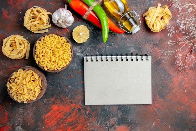 Tasty dinner preparation with uncooked pastas in various forms and garlic fallen oil bottle garlic lemon and notebook on mixed color background