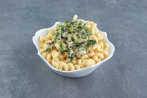 Tasty egg with greens and pasta in white bowl.