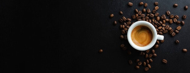 Tasty espresso served in cup with coffee beans around and spoon. view from above. dark background. banner.